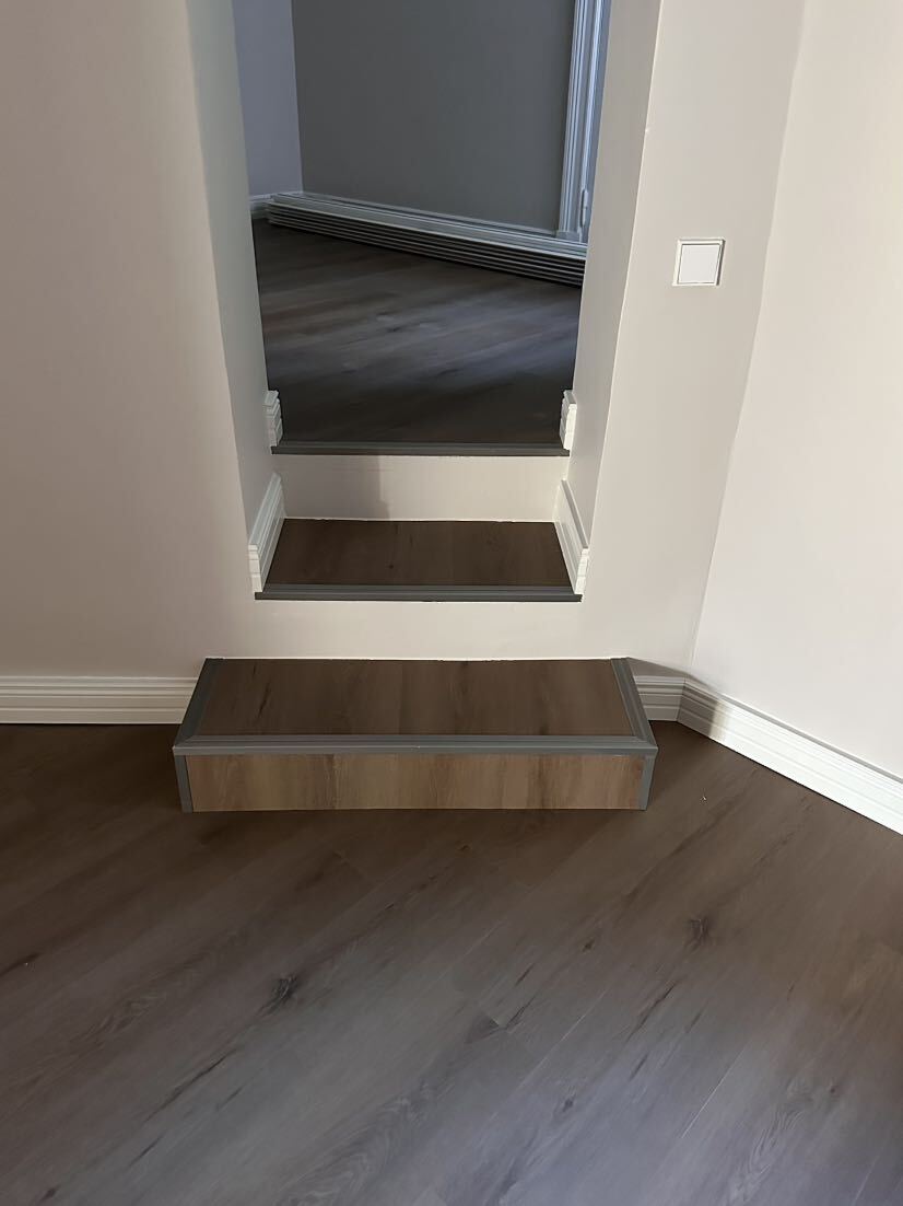 Sisäportaiden ylin askelma ja sen edessä oleva irtonainen puinen askelma, molemmat tumman puun värisiä.