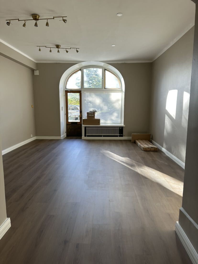 Tyhjä huone, jossa vaaleanruskeat lattialaatat, suuret kaarevat ikkunat ja muutama pahvilaatikko ikkunalaudalla ja lattialla.